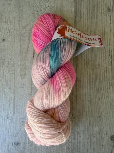 Handgefärbter Wollstrang Herzfasern No. 20 „Neonwelle Rosa“ mit leuchtendem Neonpink, zarten Rosé- und Cremetönen sowie einem kleinen türkis-grauen Farbakzent auf hellem Holzhintergrund.